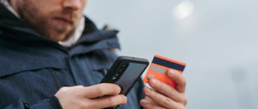 person wearing hat holding his phone and credit card in both hands