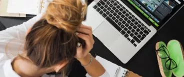 bird's eye view of person sitting in front of laptop with their head in their hands