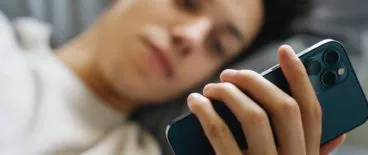 person laying in bed and looking at phone