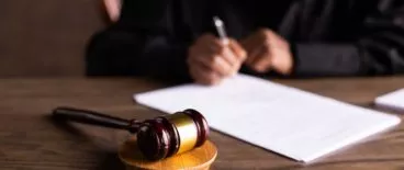 judge sitting behind wooden desk and writing on papers in front of gavel
